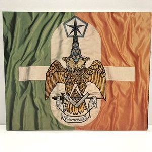 May include: A rectangular flag with a green and orange background. The flag features a central emblem with a double-headed eagle, a star, and Masonic symbols. The word "cremaster" is written on the emblem.