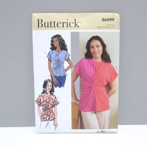 May include: Butterick sewing pattern B6899, size B5 (8-10-12-14-16), featuring illustrations and a photograph of three variations of a short-sleeve top with a front twist detail. The designs include a blue and white striped version, a floral print, and a two-tone pink and coral top.