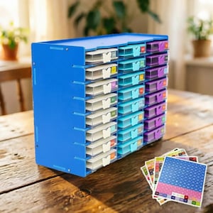 Puede incluir: Un organizador de almacenamiento de plástico azul con múltiples cajones pequeños de varios colores. Los cajones están etiquetados y tienen asas en forma de mariposa. Un conjunto de pegatinas de etiquetas coloridas está en primer plano. El organizador está sobre una superficie de madera.