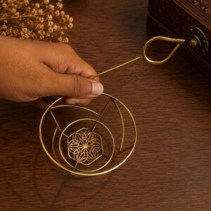 May include: A gold-toned metal tea strainer featuring a circular frame with a delicate, intricate geometric floral pattern at the base and a long, slender handle ending in a teardrop-shaped loop for easy gripping and handling during tea preparation.