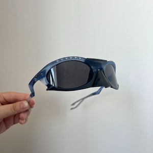 May include: Dark blue wraparound sunglasses with black lenses and a black bridge. The frames are a translucent blue with a curved shape. The arms are thin and extend to the temples. A stylish eyewear accessory.