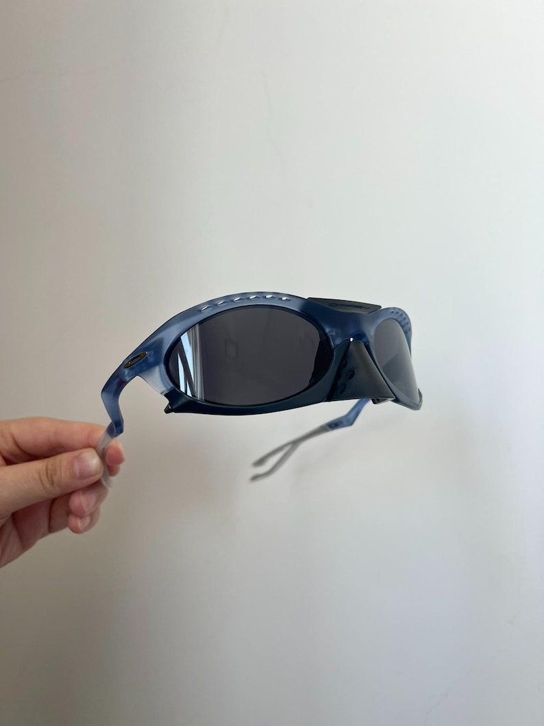 May include: Dark blue wraparound sunglasses with black lenses and a black bridge. The frames are a translucent blue with a curved shape. The arms are thin and extend to the temples. A stylish eyewear accessory.
