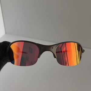 May include: Black sunglasses with red and orange reflective lenses. The sunglasses have a dark frame and a curved design. The lenses reflect a gradient of colors, including red, orange, and yellow.