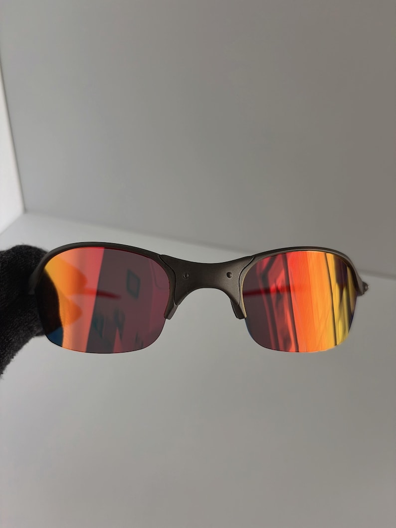 May include: Black sunglasses with red and orange reflective lenses. The sunglasses have a dark frame and a curved design. The lenses reflect a gradient of colors, including red, orange, and yellow.