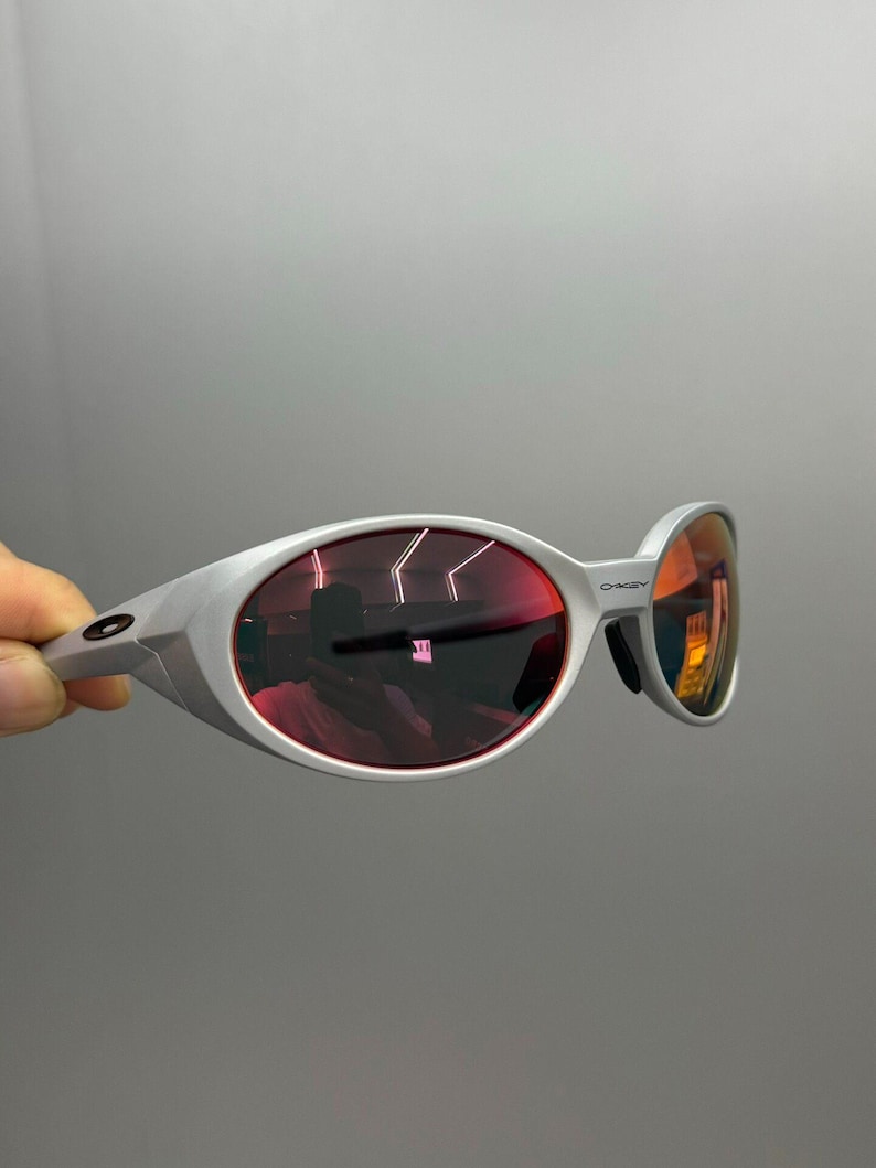 Puede incluir: Gafas de sol plateadas con lentes tintadas en rojo. Las lentes ovaladas est&aacute;n engastadas en una montura moderna. Las gafas de sol tienen un dise&ntilde;o deportivo, adecuado para actividades al aire libre.