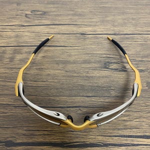 May include: A pair of sporty sunglasses with a gold-colored frame and silver accents. The temples have black rubber grips for comfort. The lenses are not visible in this image.