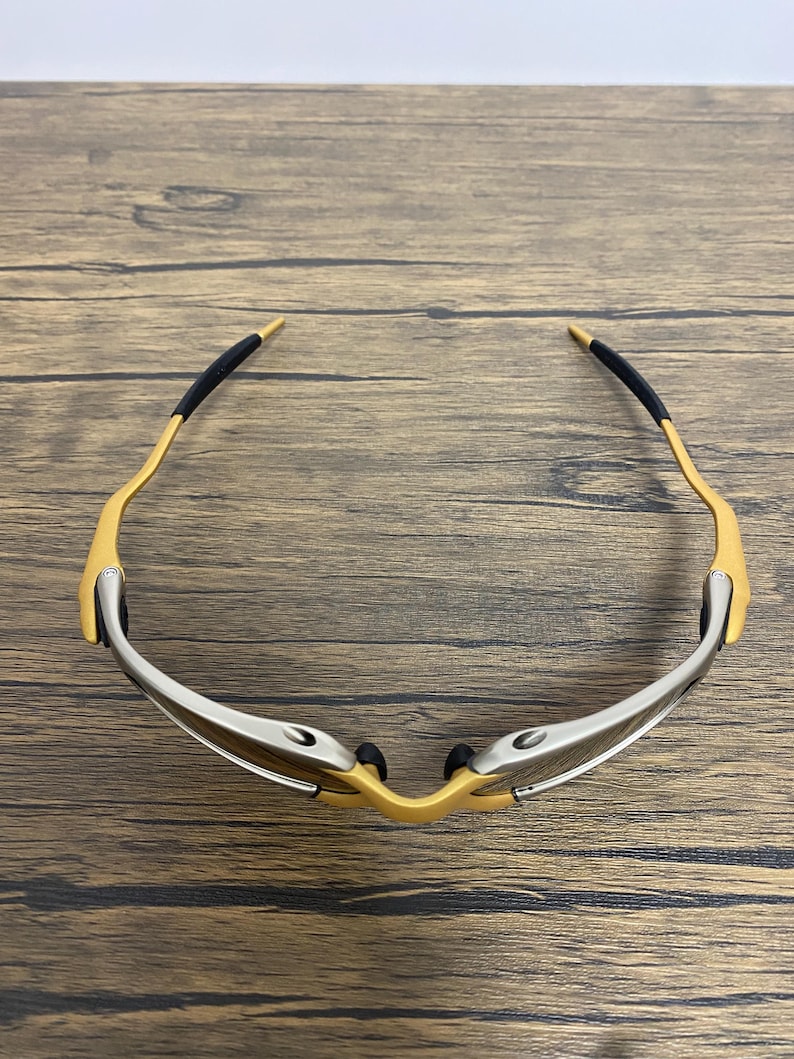 May include: A pair of sporty sunglasses with a gold-colored frame and silver accents. The temples have black rubber grips for comfort. The lenses are not visible in this image.