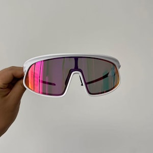 May include: White sports sunglasses with a wide frame and mirrored lenses that reflect shades of pink, orange, and purple. The sunglasses have a modern, aerodynamic design.