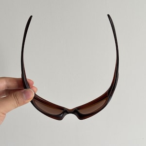 May include: Brown sunglasses with a curved frame and tinted lenses. The sunglasses have a sleek, sporty design, suitable for outdoor activities. The lenses are a warm brown colour, offering protection from the sun.