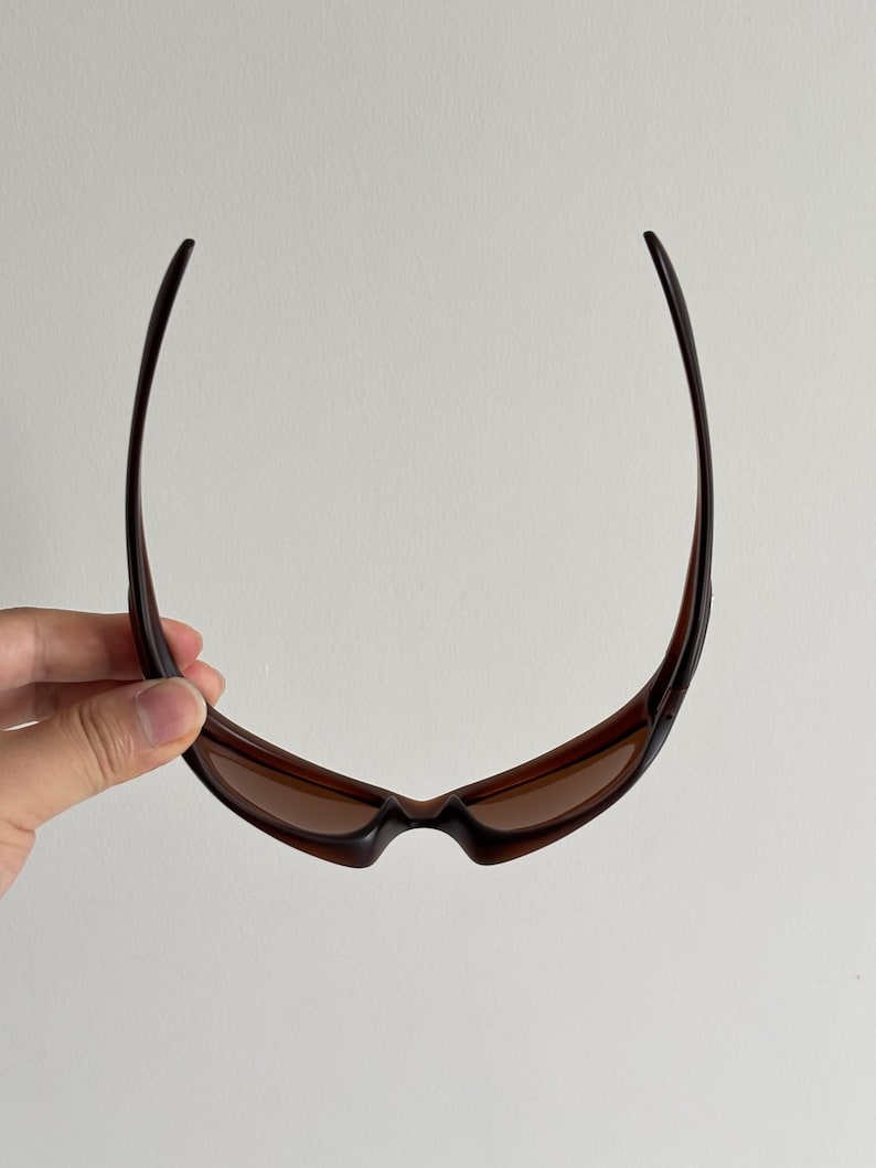 May include: Brown sunglasses with a curved frame and tinted lenses. The sunglasses have a sleek, sporty design, suitable for outdoor activities. The lenses are a warm brown colour, offering protection from the sun.