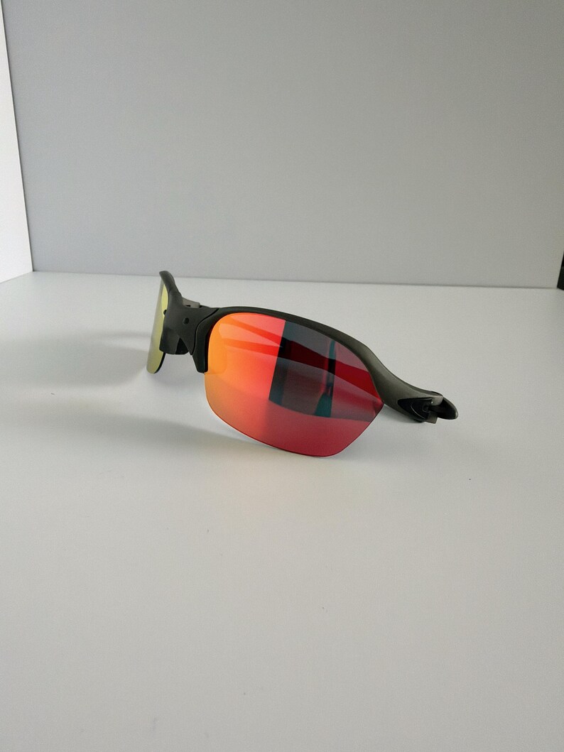 May include: Black sunglasses with red and orange gradient lenses. The sunglasses have a sleek, modern design with a black frame and a curved shape. The lenses transition from red to orange, offering a stylish look.