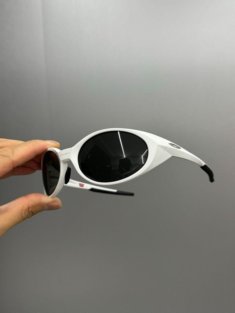 K&ouml;nnte beinhalten: Wei&szlig;e Sonnenbrille mit gro&szlig;en, ovalen Gl&auml;sern und einem schlanken Design. Die Rahmen sind wei&szlig; mit schwarzen Akzenten an den B&uuml;geln. Die dunklen Gl&auml;ser bilden einen Kontrast zu den wei&szlig;en Rahmen. Ein stilvolles Accessoire zum Schutz der Augen.
