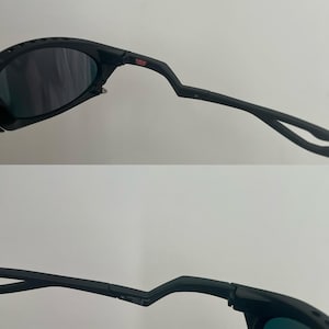 Może przedstawiać: Czarne okulary przeciwsłoneczne z ciemnymi soczewkami. Oprawki mają unikalny, kanciasty design z małym czerwonym logo "USA". Zausznik jest zakrzywiony i posiada zawias. Og&oacute;lny styl jest sportowy.