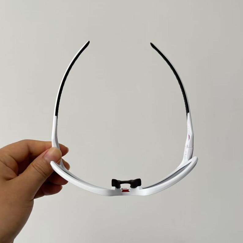May include: White sports sunglasses with black accents. The sunglasses have a sleek, modern design with a curved frame and dark lenses. The arms are white with black detailing. The bridge features a black piece with a red accent.
