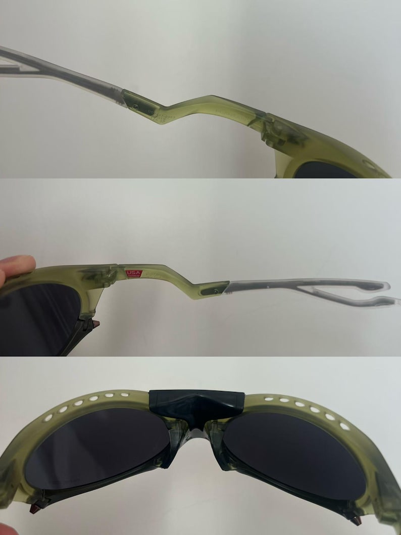 May include: Olive green sunglasses with dark lenses. The frames have a unique, angular design with a bridge and temples. The sunglasses have a small "USA" label on the frame.