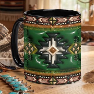 May include: Black ceramic mug with a Southwestern design. The mug has a black handle and rim, with a vibrant green center adorned with a geometric pattern in black, white, and brown. The design includes a central cross-like motif and decorative borders.
