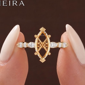 May include: A gold ring setting featuring a central marquise-shaped frame with an X-shaped interior structure. The band is adorned with alternating marquise and round cut white stones. The word MEIRA is printed in the top left corner of the image.