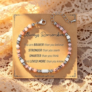 Könnte beinhalten: Ein Armband mit rosa und silberfarbenen Perlen, präsentiert auf einer Karte mit dem Text "Always Remember". Die Karte enthält auch die Sätze "You are BRAVER than you believe" und "Handmade with Love."