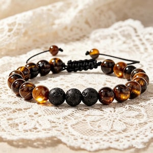 May include: A beaded bracelet featuring a mix of brown tiger eye and black lava stone beads. The bracelet has a black adjustable cord closure. The beads are round and vary in shades of brown and black.