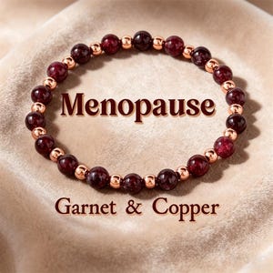May include: A beaded bracelet featuring deep red garnet stones and copper-colored beads. The text "Menopause" and "Garnet & Copper" are displayed on the image. The bracelet is presented on a soft, neutral-toned surface.