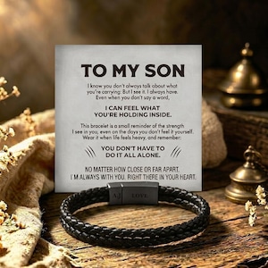 May include: A black braided leather bracelet with a rectangular metal clasp featuring the engraved letters A.J. and the word LOVE, displayed in front of a white card with the printed text TO MY SON and a message about strength and support.
