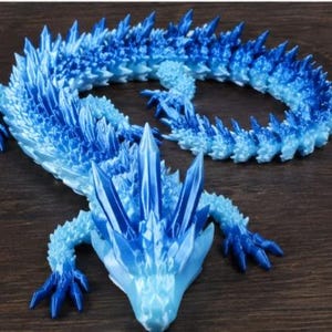 Op de afbeelding: Een gearticuleerd drakenfiguur met een kleurverloop dat varieert van lichtblauw tot diep koningsblauw. Het wezen heeft een getextureerd, kristallijn uiterlijk met scherpe, puntige schubben langs de rug en de kop.
