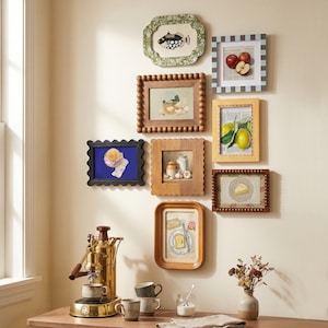 May include: A gallery wall arrangement featuring eight diverse rectangular and scalloped picture frames containing various food and nature illustrations, positioned above a brass espresso machine, ceramic mugs, and a small vase with dried flowers.
