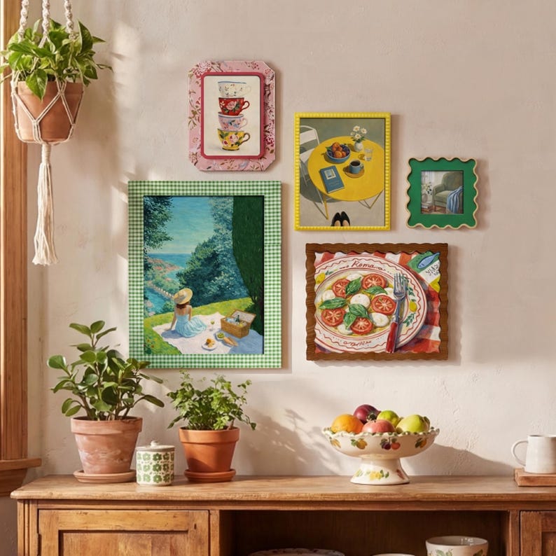 May include: A gallery wall arrangement featuring five framed art prints: a stack of teacups, a yellow table with fruit, a green-framed landscape with a person on a picnic, a scalloped green frame, and a plate of caprese salad labeled Roma.