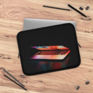 May include: Black laptop sleeve with a colorful image of a laptop keyboard. The sleeve is on a wooden surface with pencils, a pen, and binder clips.