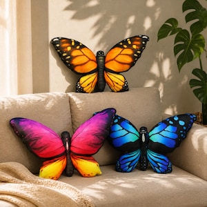 May include: Three butterfly-shaped scatter cushions. The top cushion features orange and black wings. The bottom left cushion displays a gradient of pink, purple and yellow. The bottom right cushion showcases vibrant blue and black wing patterns.