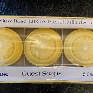 May include: A box of yellow, round guest soaps. Each soap has a floral design in the center and a decorative border. The box is labeled "Yellow Rose Luxury French Milled Soaps" and "Guest Soaps."