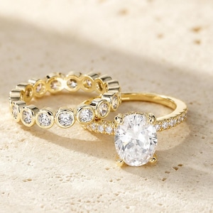 Peut inclure: Un ensemble de deux bagues en or. L'une présente une grande pierre claire taille ovale sur un anneau pavé, tandis que la seconde est une alliance tour complet composée de multiples pierres claires rondes serties dans des chatons en or.