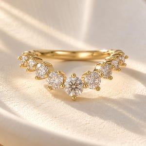 Peut inclure: Une bague en or en forme de V ornée d'une série de onze pierres rondes, transparentes et facettées, serties sur la bande. La pierre centrale est la plus grande, les pierres diminuant progressivement vers chaque extrémité de la bande incurvée.
