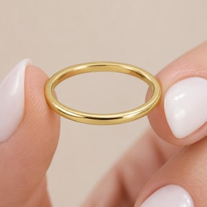Puede incluir: Un anillo de banda de oro fino y pulido con una superficie lisa y redondeada. El anillo presenta un diseño circular continuo con un acabado metálico de alto brillo, mostrando una apariencia limpia y uniforme en toda su circunferencia.
