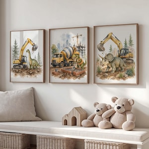 Op de afbeelding: Drie ingelijste aquarelprints met bouwmachines en dinosaurussen. Elke print heeft een bruine lijst. Eén toont een gele graafmachine met een Brontosaurus, een andere een betonmixer met dinosaurussen en de laatste een Triceratops met een graafmachine.