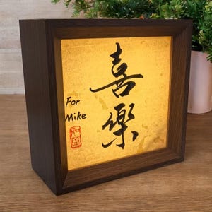 May include: A dark brown wooden framed light box with a gold-colored interior. The box features black calligraphy and the words "For Mike" in English. A red stamp is visible below the text.