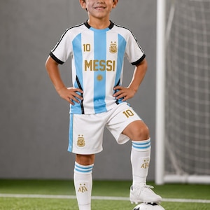 May include: A white and light blue striped soccer jersey with the name MESSI and the number 10 in gold, paired with white shorts featuring the number 10 and the AFA logo, and white soccer socks with blue stripes and the AFA logo, worn with white cleats.