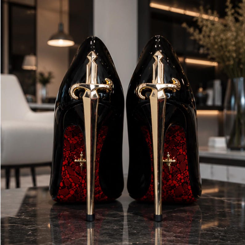 May include: A pair of black high-heeled shoes featuring a glossy finish and a gold-toned metal sword-shaped heel. The underside of the sole displays a vibrant red lace-like pattern with a small gold cross emblem embedded in the center of the arch.