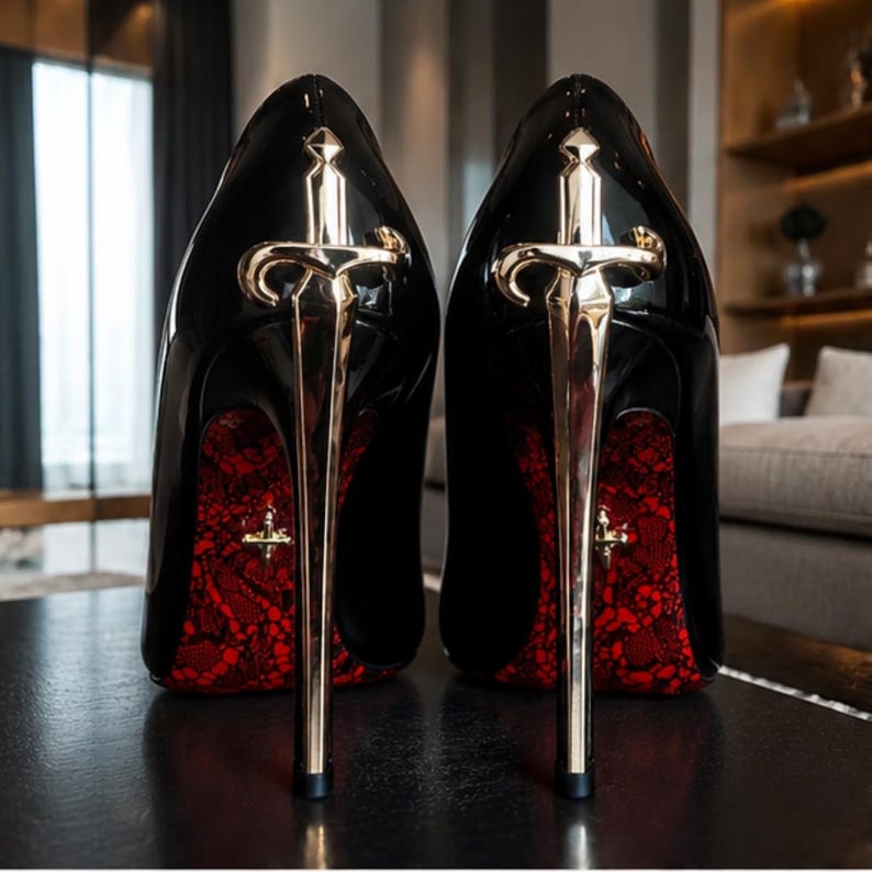 May include: A pair of black patent leather high-heeled pumps featuring a metallic gold sword-shaped stiletto heel. The interior lining of the shoes displays a vibrant red lace pattern, and a small gold cross emblem is visible on the inner heel.