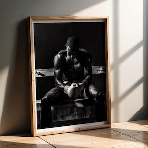 Può includere: Stampa in bianco e nero incorniciata di un pugile che riposa su una panchina. Il pugile indossa guantoni da boxe ed è seduto con la testa china. L'immagine è in una cornice di legno e si appoggia a un muro.