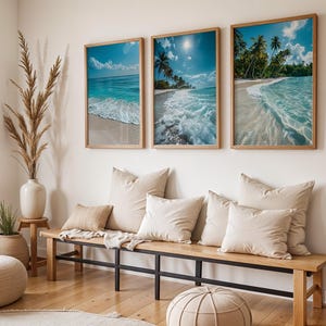 Puede incluir: Tres impresiones enmarcadas de escenas de playa con agua turquesa, arena blanca y palmeras cuelgan sobre un banco de madera con cojines beige. Un jarrón con hierba seca alta y una pequeña planta en maceta se encuentran cerca, creando un tema costero.