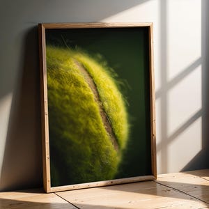Può includere: Stampa incorniciata con un primo piano di una pallina da tennis. La pallina è di un giallo-verde brillante con una cucitura marrone. La cornice in legno aggiunge un tocco naturale e l'immagine è ambientata su uno sfondo verde scuro.