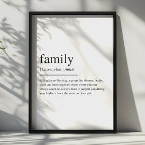 Könnte beinhalten: Ein schwarz gerahmter Kunstdruck mit einer wörterbuchartigen Definition des Wortes family. Der Text enthält die phonetische Aussprache fam-uh-lee, die Klassifizierung als Substantiv und einen beschreibenden Absatz über die Familie als Segen.