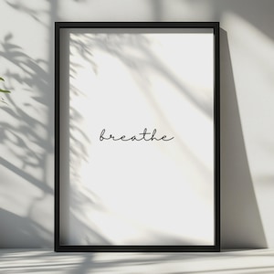 May include: A rectangular wall art print encased in a thin black frame. The print features a white background with the word breathe written in a simple, lowercase black cursive script centred in the middle of the frame.