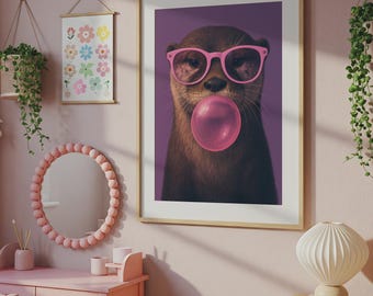 May include: A framed wall art print featuring a brown otter wearing bright pink glasses and blowing a large pink bubble gum bubble, set against a solid purple background. The artwork is displayed in a light wood frame on a soft pink wall.