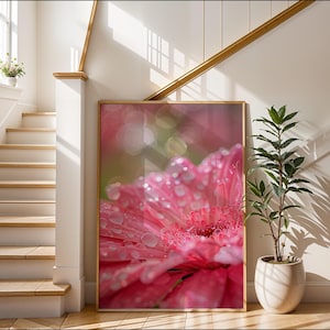 May include: A rectangular framed wall art print featuring a close-up of a vibrant pink gerbera daisy flower covered in clear water droplets. The petals are saturated in shades of magenta and pink, with a soft, blurred bokeh background effect.