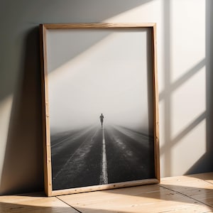 Può includere: Fotografia in bianco e nero incorniciata che raffigura una persona che corre lungo una strada lunga e dritta. La strada è segnata da una linea bianca centrale e la scena è avvolta nella nebbia. La cornice è in legno chiaro.