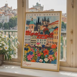 May include: A framed art print titled Flower Market Prague 2024 featuring a colorful illustration of the Prague cityscape with red-roofed buildings and a vibrant foreground of various flowers in shades of pink, blue, yellow, and white.