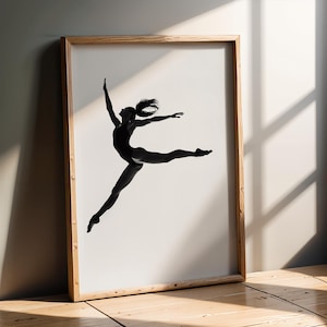 Può includere: Stampa in bianco e nero di una ballerina in movimento. La ballerina, in un body, è raffigurata in un salto, con braccia e gambe tese. La cornice in legno chiaro è appoggiata a una parete neutra.