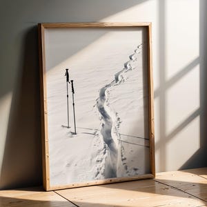 Può includere: Fotografia in bianco e nero incorniciata di un paesaggio innevato. Un sentiero di impronte taglia la neve, conducendo verso l'orizzonte. Due bastoncini da sci sono piantati nella neve, aggiungendo profondità alla scena invernale.